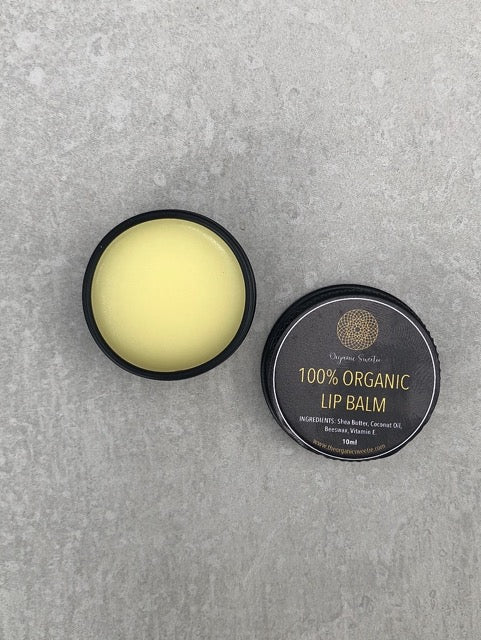 Organic Sweetie 100% organic lip balm displayed on table showing the lid label and a creamy mixture inside of tin. Tin lid is displaying the ingredients that are used in this natural lip balm - Shea Butter, Coconut Oil, Beeswax, Vitamin E. All ingredients are 100% certified organic.